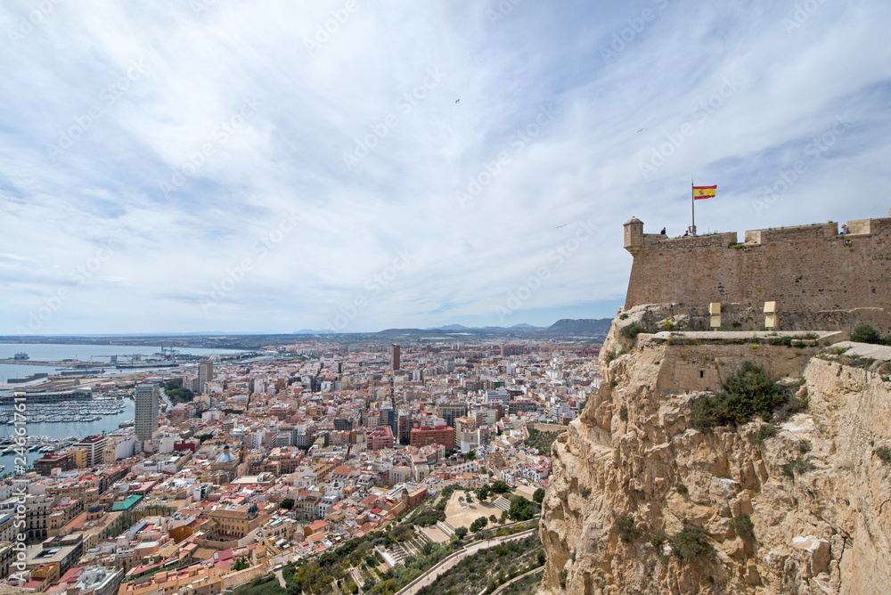 Wide angle view of Alicante, Spain from castle of Santa Barbara. Panoramic view of Postiguet beach, city and harbor. Mixed view of modern city and ruined fortress walls and towers.  