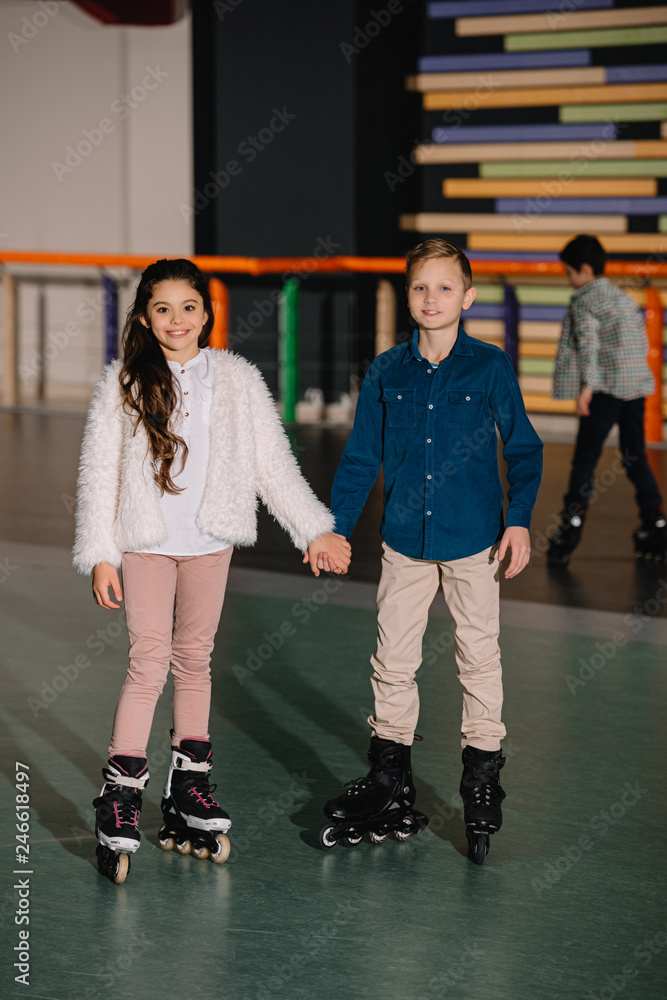 Fototapeta premium Two beautiful smiling children in roller skates standing with holding hands
