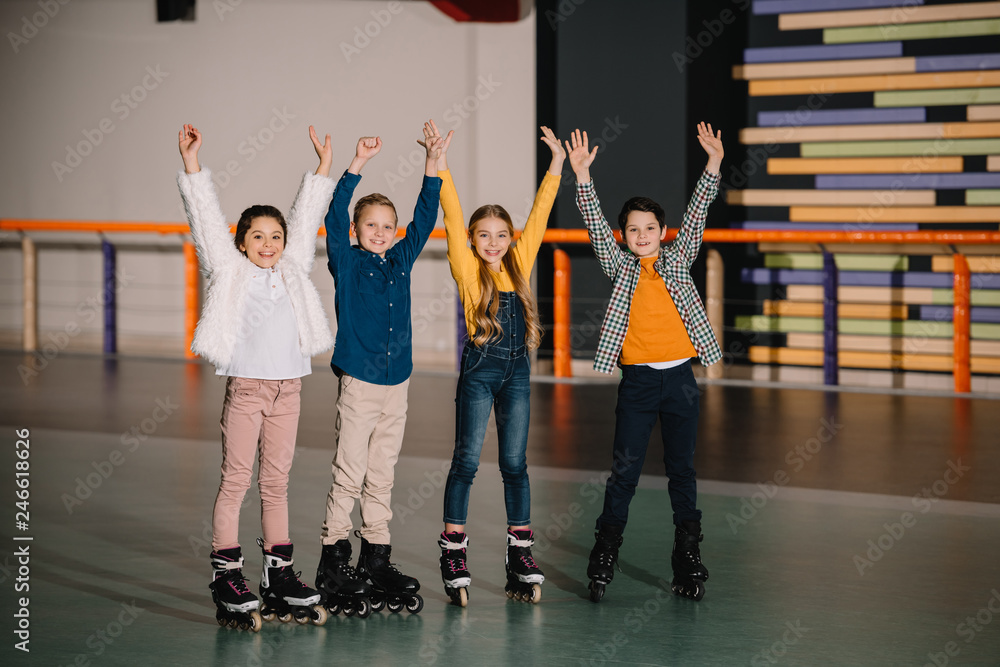Happy smiling children in roller skates standing in spacious roller rink with hands up