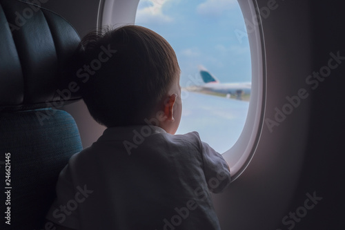 Curious cute little Asian 2 -3 years old toddler baby boy child looking out from airplane window during flight on airplane. Flying with children, Happy air travel with kids & little traveler concept © yAOinLoVE