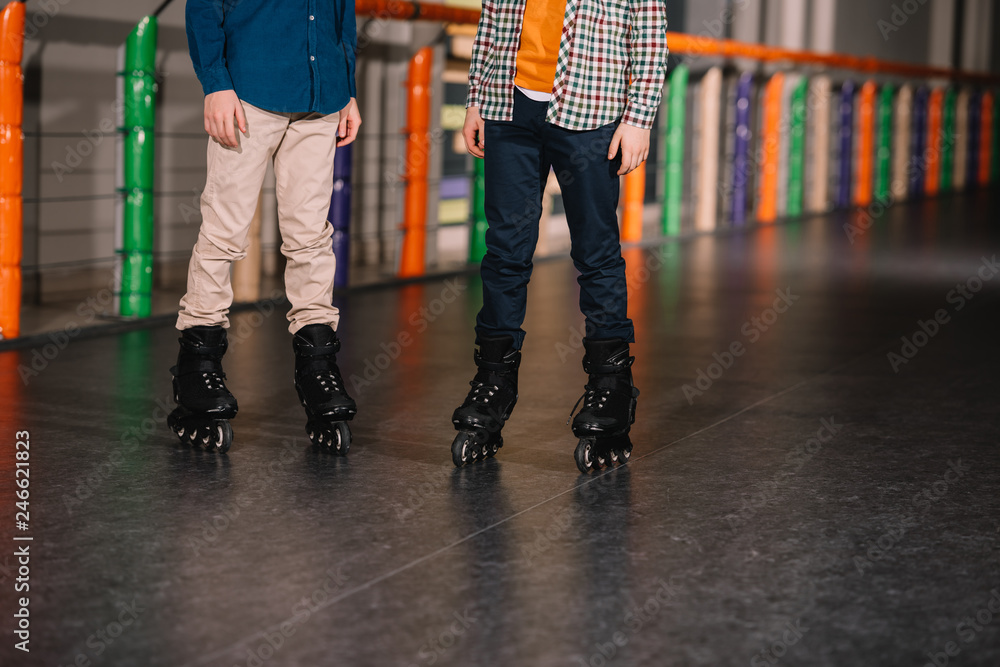 Obraz premium Partial view of boys in black roller skates posing on rink