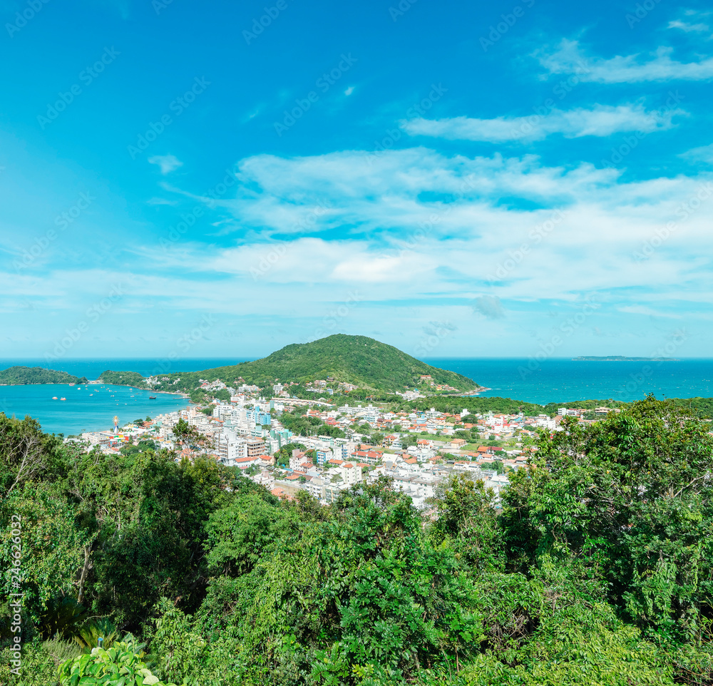 Bombinhas - SC, Brazil. Panoramic view of the touristic city of Bombinhas and some beaches with blue sea around the hill. Coastal city on a beautiful sunny day.