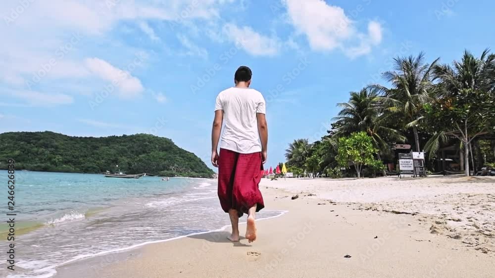 A young, handsome man is walking along the beach on a tropical island.