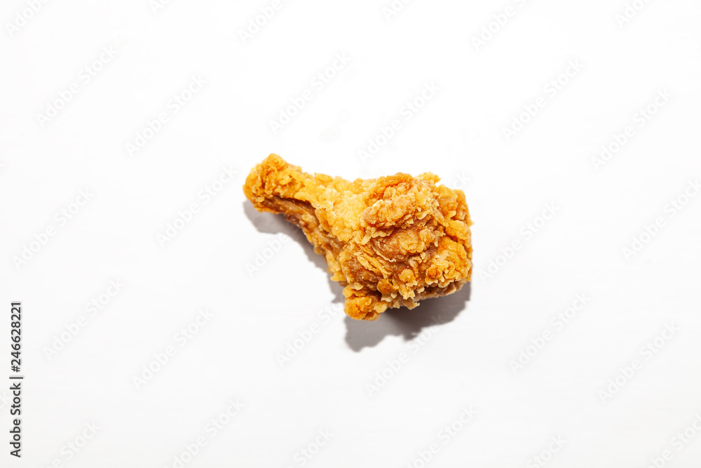 Close-up of one fried fatty appetizing chicken wing in a brown flour breading on a white background, unhealthy fatty food causing a disease with elevated cholesterol.