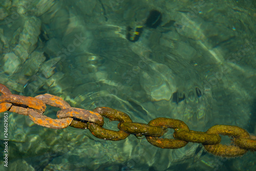 Old massive rusty chain dipping into clear sea water in harbor