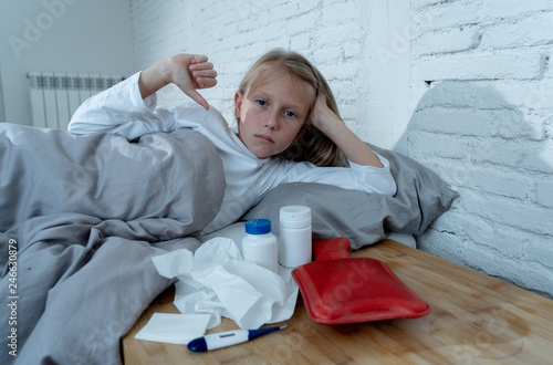 Little girl lying sick in bed checking thermometer having high fever and cold flu symptoms