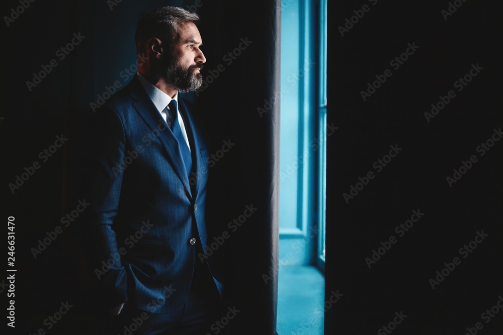 Thinking about... Thoughtful man in full suit looking away through the window while standing indoors. Thinking about... Thoughtful man in full suit looking away through the window while standing indoors.