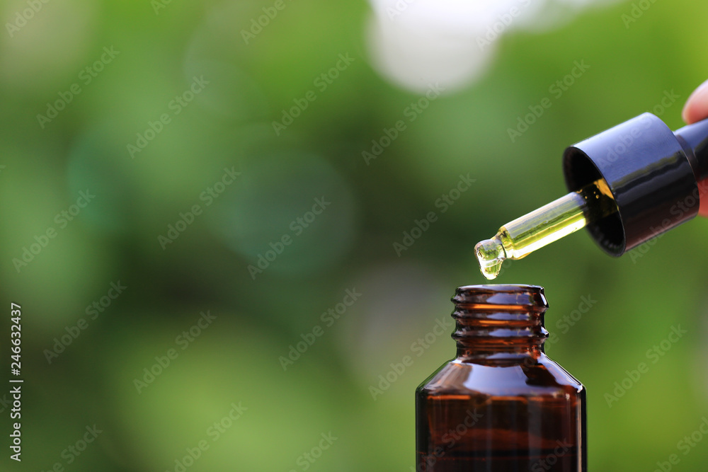 Woman hand holding essential oil or vitamin C dropping to the bottle on natural green background, Cosmetic pipette and spa concept Woman hand holding essential oil or vitamin C dropping to the bottle on natural green background, Cosmetic pipette and spa concept