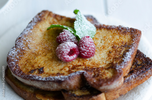 Close up of French toast, making with bread soaked in eggs and milk, then fried , served with icing sugar and raspberries with mint.