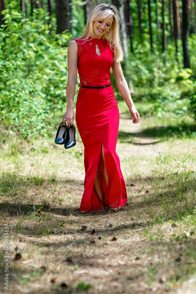 Beautiful blonde woman in red dress and black shoes in hand walks through the forest. Beautiful blonde woman in red dress and black shoes in hand walks through the forest.