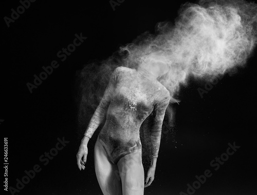 Beautiful slim girl wearing a gymnastic bodysuit covered with white powder and dust flies from her hair on a dark. Artistic conceptual black and white photo.