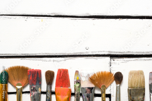 Artist's tools, dirty brushes in paint lie in a row on a white wooden background. Abstract conceptual background with place for text.