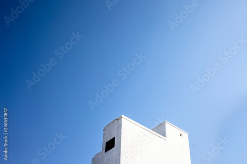 Architectural minimalistic shot of white colored building with sun and clouds and a sun flair.