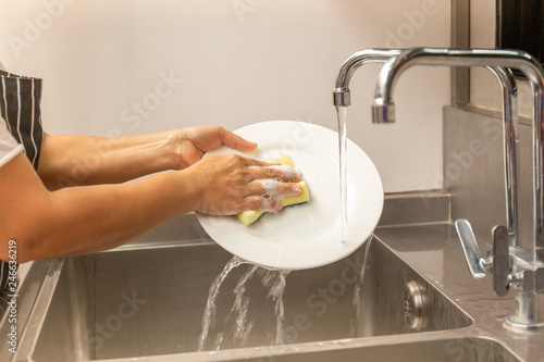 Hands washing dirty dishes with running water in kitchen sink. photo