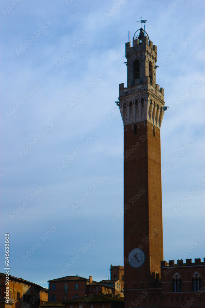 Mangia tower (torre del Mangia), symbol of Siena, with clock on the winter blue sky background, Tuscany, Italy