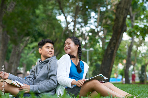 Cheerful mixed-raced kids resting on campus and reading books