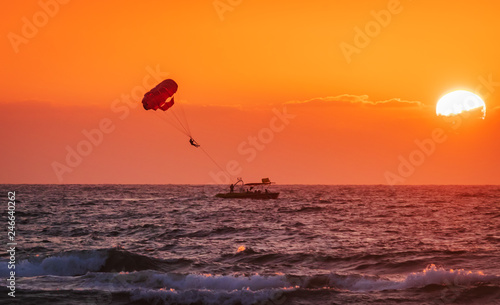 amazing shot at sunset of Parasailing water amusement - flying on a parachute behind a boat on a summer holiday by the sea in the resort Baga beach Goa India