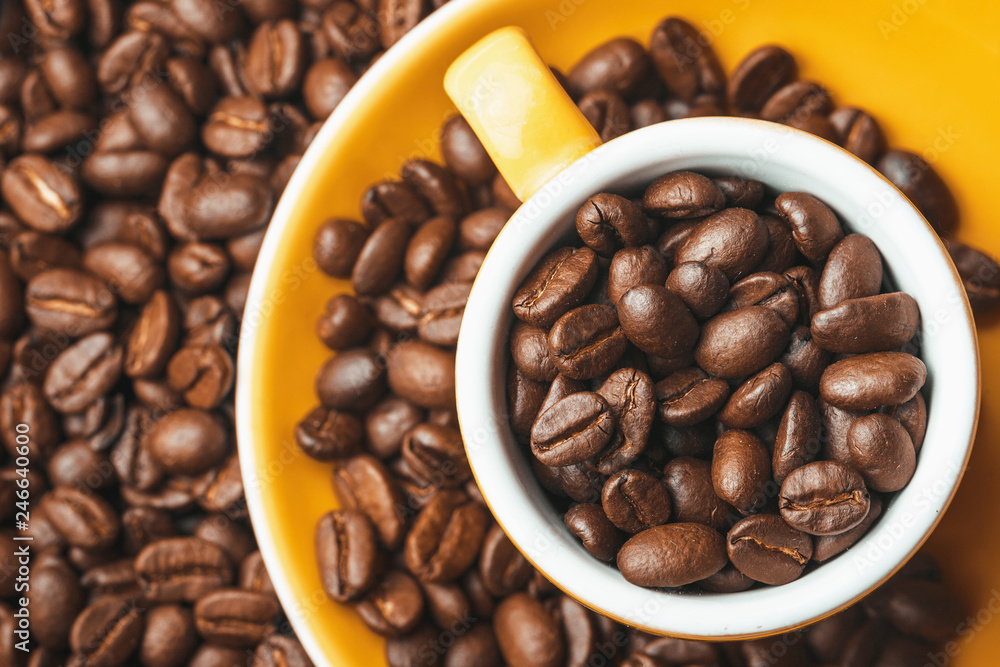 Fototapeta premium Yellow orange small espresso cup with coffee seeds inside and around.