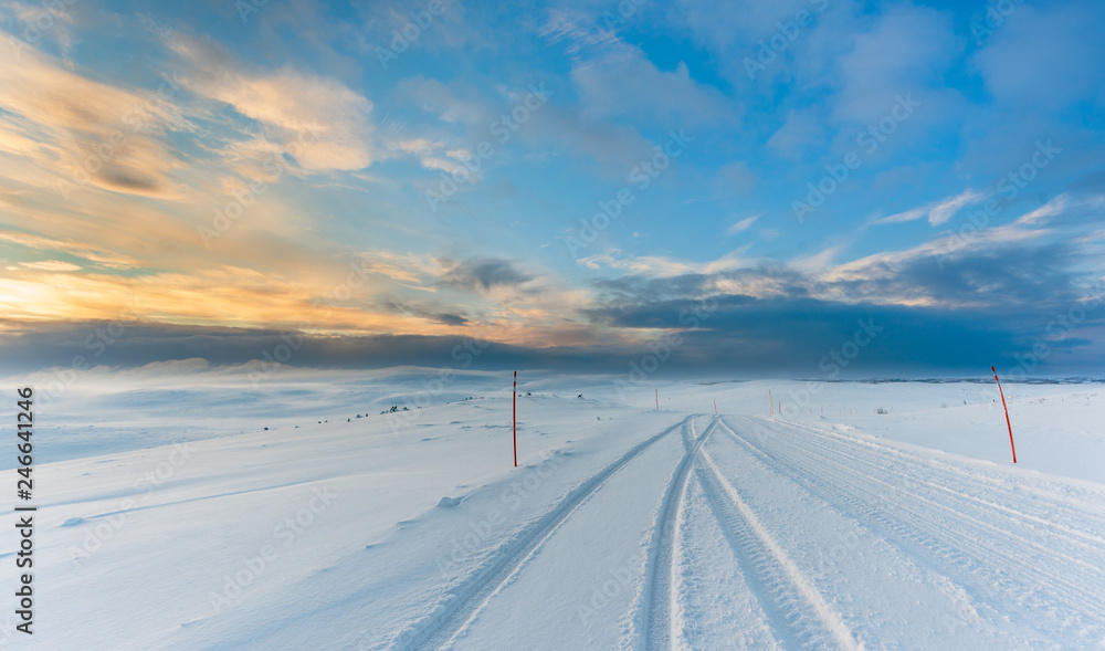 Epic Arctic Road trip. Ice Road with tire tracks on snow in Arctic landscape with the blue sky starting to turn gold as the sunset approaches. 