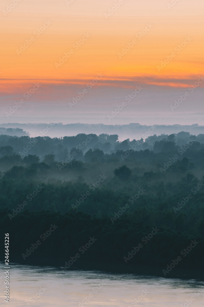 Mystical view on riverbank of large island with forest under haze at early morning. Mist among layers from tree silhouettes under warm predawn sky. Morning atmospheric landscape of majestic nature. Mystical view on riverbank of large island with forest under haze at early morning. Mist among layers from tree silhouettes under warm predawn sky. Morning atmospheric landscape of majestic nature.