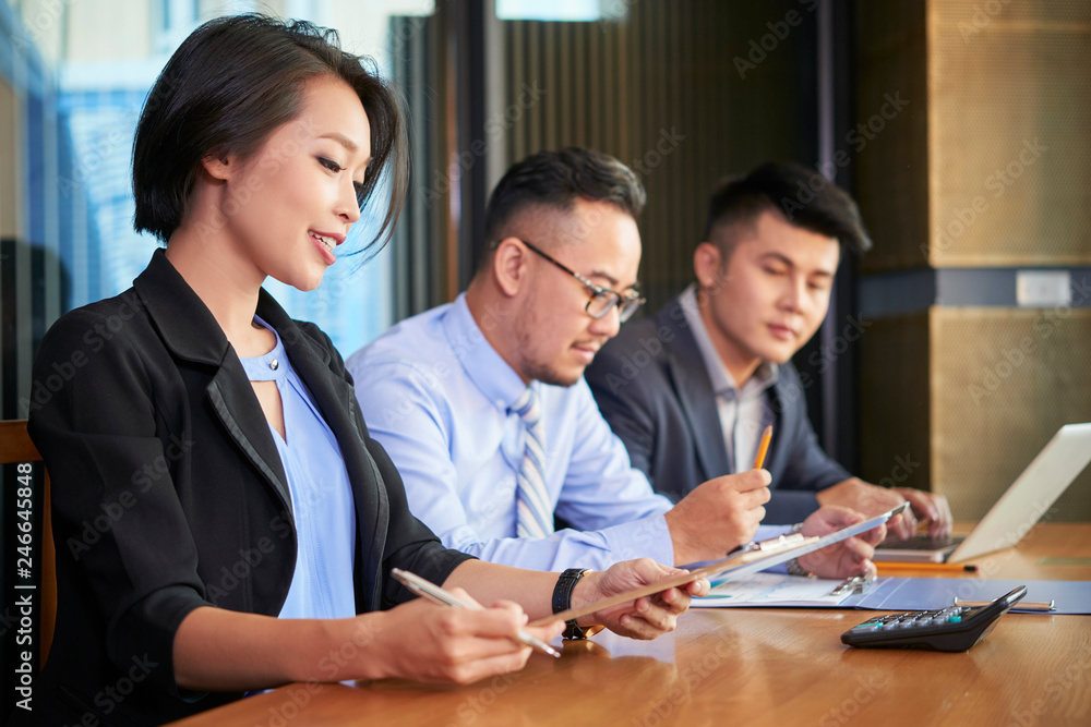 Young Vietnamese business lady reading contract at meeting with business partners Young Vietnamese business lady reading contract at meeting with business partners