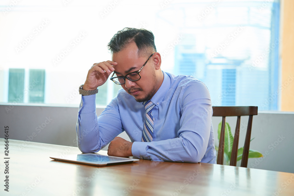Vietnamese entrepreneur concentrated on reading document on digital tablet Vietnamese entrepreneur concentrated on reading document on digital tablet