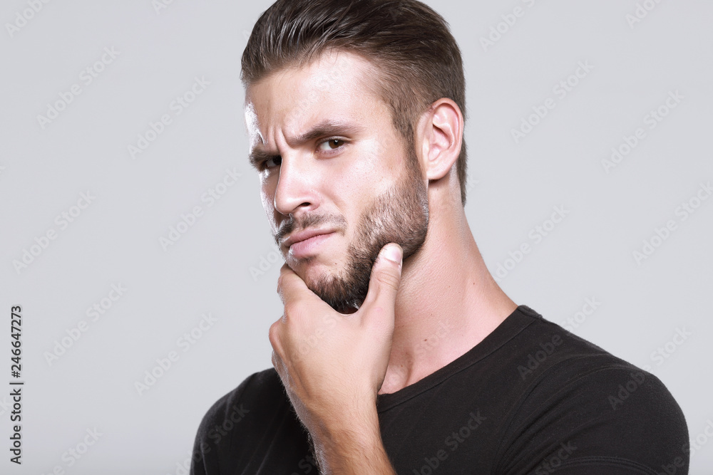 Muscular model young man with beard in black t-shirt on gray background. Fashion portrait of brutal sporty sexy strong muscle guy with modern trendy hairstyle. Model, fashion concept. Muscular model young man with beard in black t-shirt on gray background. Fashion portrait of brutal sporty sexy strong muscle guy with modern trendy hairstyle. Model, fashion concept.