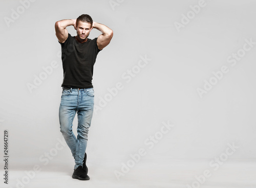 Muscular model sports young man in jeans and black t-shirt on a grey background. Fashion portrait of brutal sporty healthy strong muscle guy with a modern trendy hairstyle.