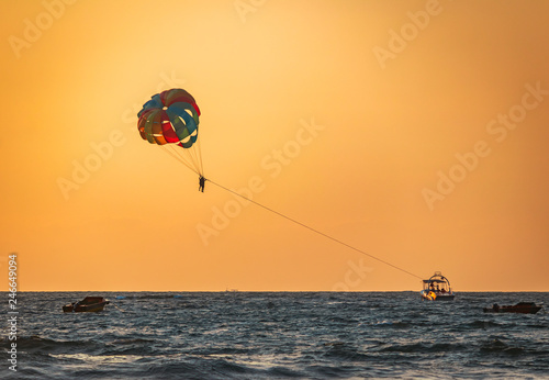 amazing shot at sunset of Parasailing water amusement - flying on a parachute behind a boat on a summer holiday by the sea in the resort Baga beach Goa India