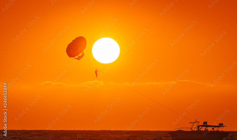amazing shot at sunset of Parasailing water amusement - flying on a parachute behind a boat on a summer holiday by the sea in the resort Baga beach Goa India amazing shot at sunset of Parasailing water amusement - flying on a parachute behind a boat on a summer holiday by the sea in the resort Baga beach Goa India