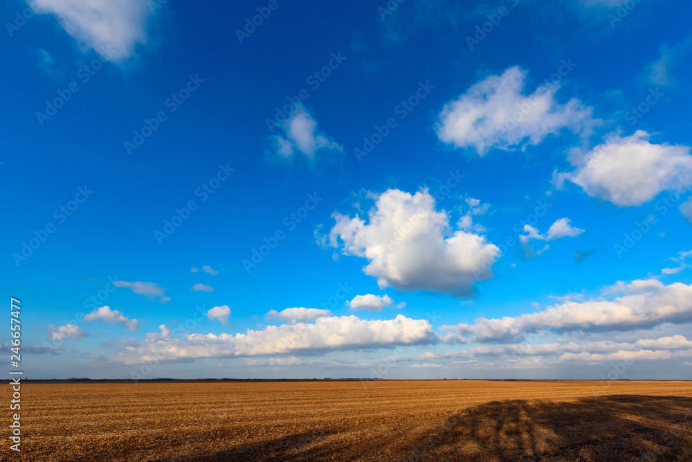 White clouds are crossing blue sky over plain landscape White clouds are crossing blue sky over plain landscape