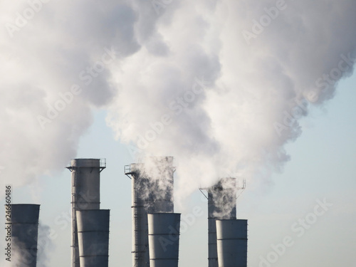 Air pollution, industrial smoke from chimneys on blue sky background. Factory pipes, concept of industry and ecology, steam plant, heating season, global warming