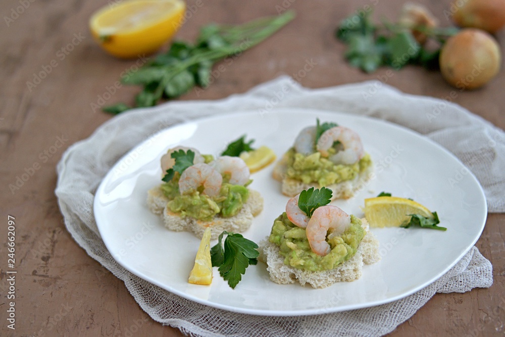 Small snack sandwiches on white bread with guacamole and shrimps on a white plate. Selective focus. Small snack sandwiches on white bread with guacamole and shrimps on a white plate. Selective focus.