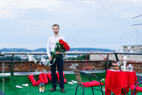 man with big bouquet of red roses waiting for his wife to surpri photo