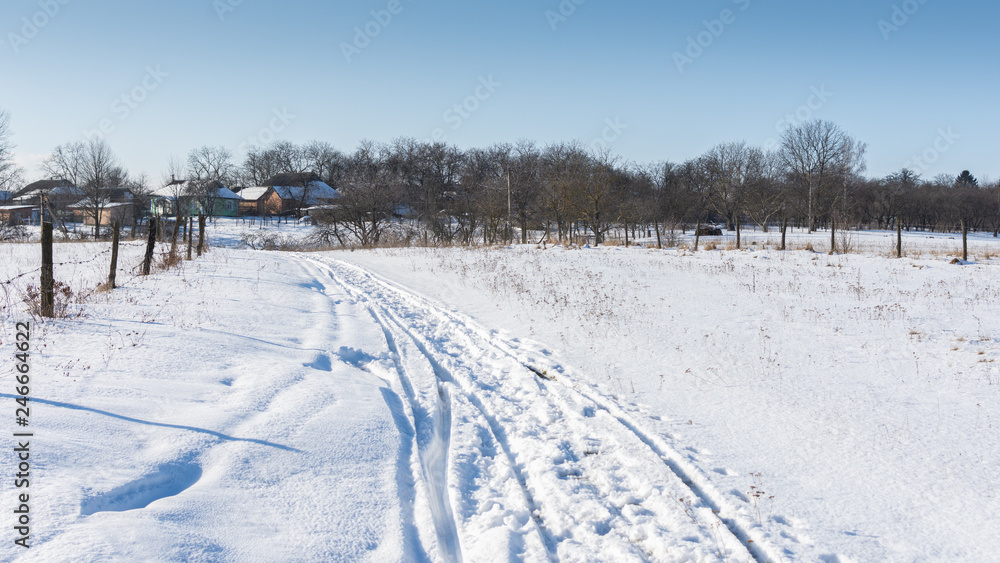 Fototapeta premium Road along the snow-covered fields to the village, winter time