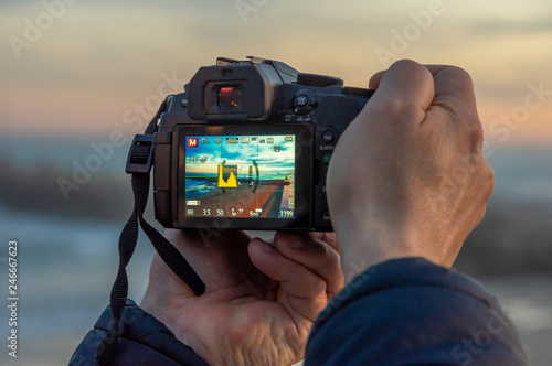 Man hands taking a photograph with DSLR of sunset landscape