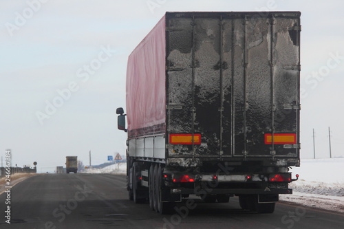 Back view on dirty european semi-trailer truck on asphalt winter road - speed delivery, traffic