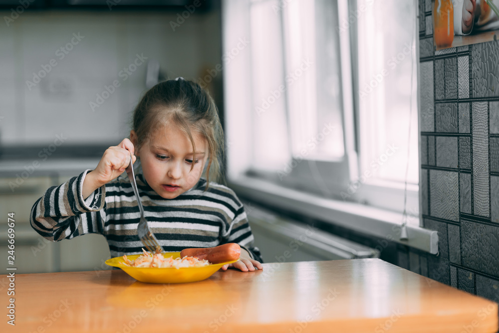 girl eating pasta with sausage in the kitchen in a striped jacket girl eating pasta with sausage in the kitchen in a striped jacket