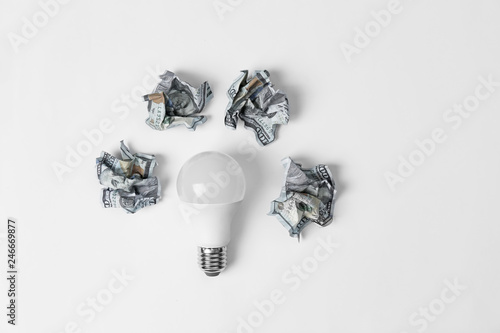 Fototapeta Naklejka Na Ścianę i Meble -  Composition with lamp bulb and crumpled banknotes on white background, top view. Creative concept
