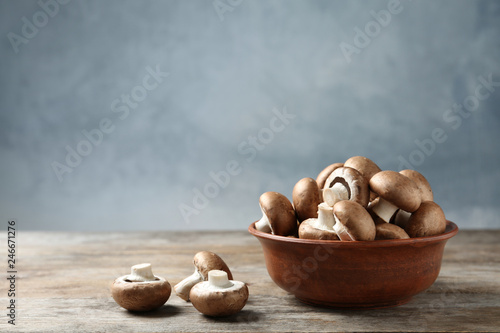 Fresh champignon mushrooms and bowl on wooden table, space for text