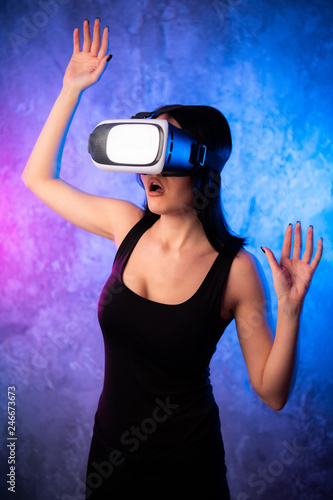 Wondering Young Woman in Virtual Reality Glasses over neon colored background. Shocked Girl wearing VR device. Close-up portrait of Female with VR headset. © romankosolapov