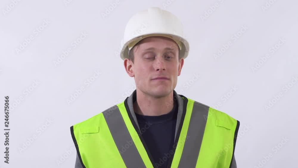 Young handsome self confident man stand in white background and fixing his construction hat. Shooting in the studio on a white background. Young handsome self confident man stand in white background and fixing his construction hat. Shooting in the studio on a white background.