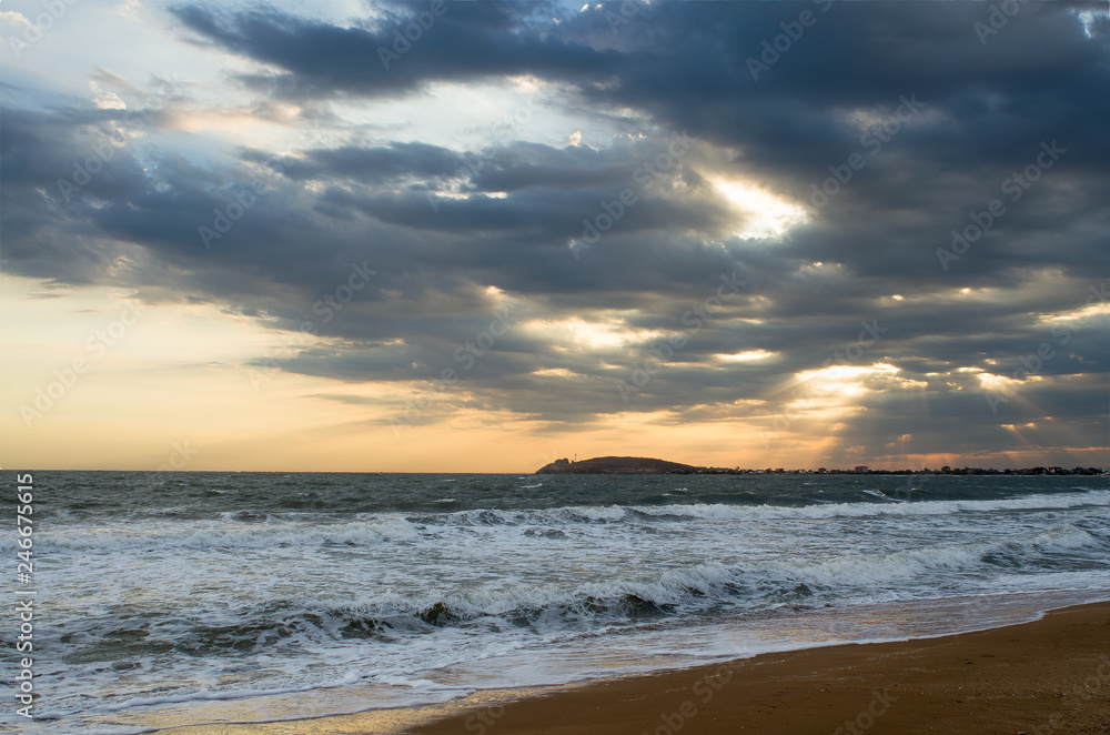 Evening on the beach, the waves wash the sandy beach, the sunset sky picturesque clouds on the horizon, the far coast.