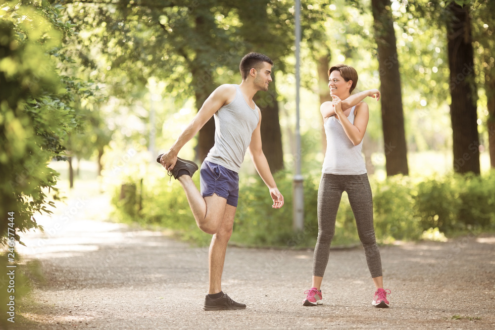 Beautiful happy couple doing together stretching exercises outdoors