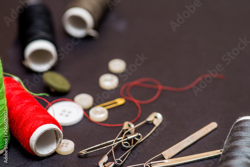 spools of thread, pins, needles, buttons and other tools scattered on a dark background