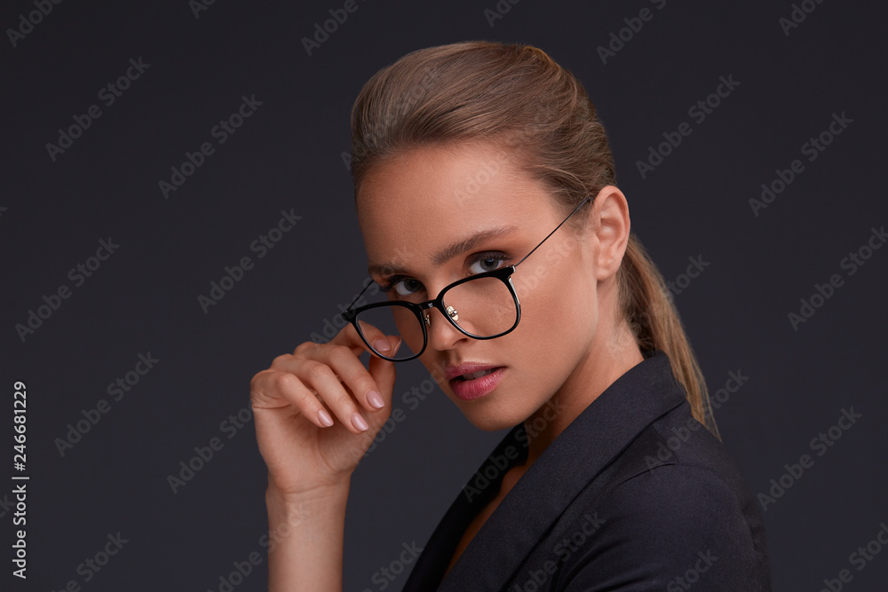 Elegant serious woman in square eyeglasses looking at camera on dark background.Adult beautiful businesswoman in jacket.Black frame spectacles.Vision correction,optical shop,glasses store concept. Elegant serious woman in square eyeglasses looking at camera on dark background.Adult beautiful businesswoman in jacket.Black frame spectacles.Vision correction,optical shop,glasses store concept.