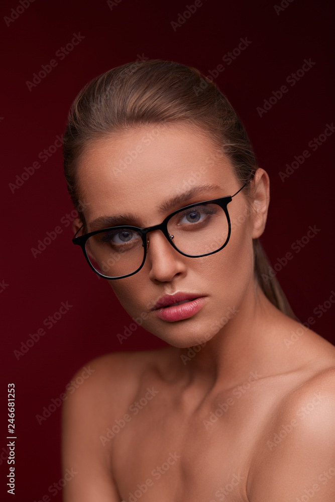 Attractive woman in square eyeglasses looking at camera on red background. Portrait of young beautiful blonde girl.Black frame spectacles.Vision correction,optical shop,glasses store,eyewear concept. Attractive woman in square eyeglasses looking at camera on red background. Portrait of young beautiful blonde girl.Black frame spectacles.Vision correction,optical shop,glasses store,eyewear concept.