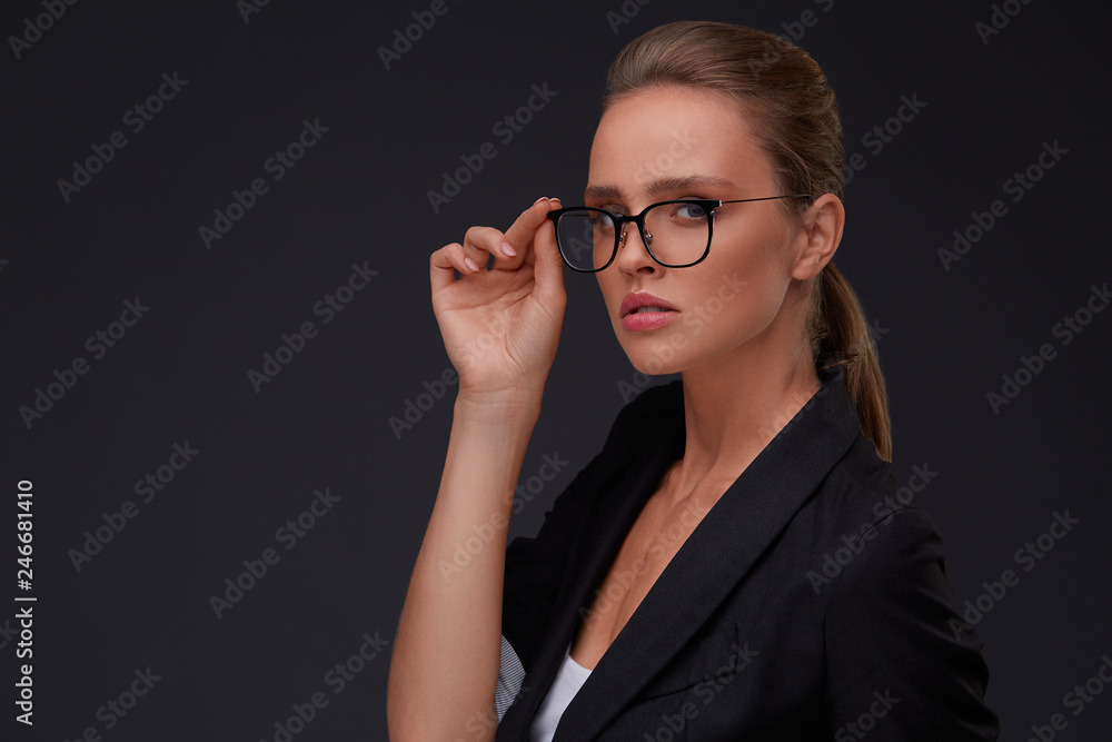 Elegant serious woman in square eyeglasses looking at camera on dark background.Adult beautiful businesswoman in jacket.Black frame spectacles.Vision correction,optical shop,glasses store concept. Elegant serious woman in square eyeglasses looking at camera on dark background.Adult beautiful businesswoman in jacket.Black frame spectacles.Vision correction,optical shop,glasses store concept.
