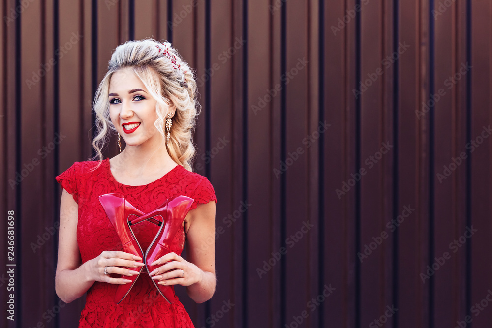 attractive young blonde in a red dress holds in hands red shoes. attractive young blonde in a red dress holds in hands red shoes.