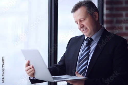 confident businessman with laptop standing in office.